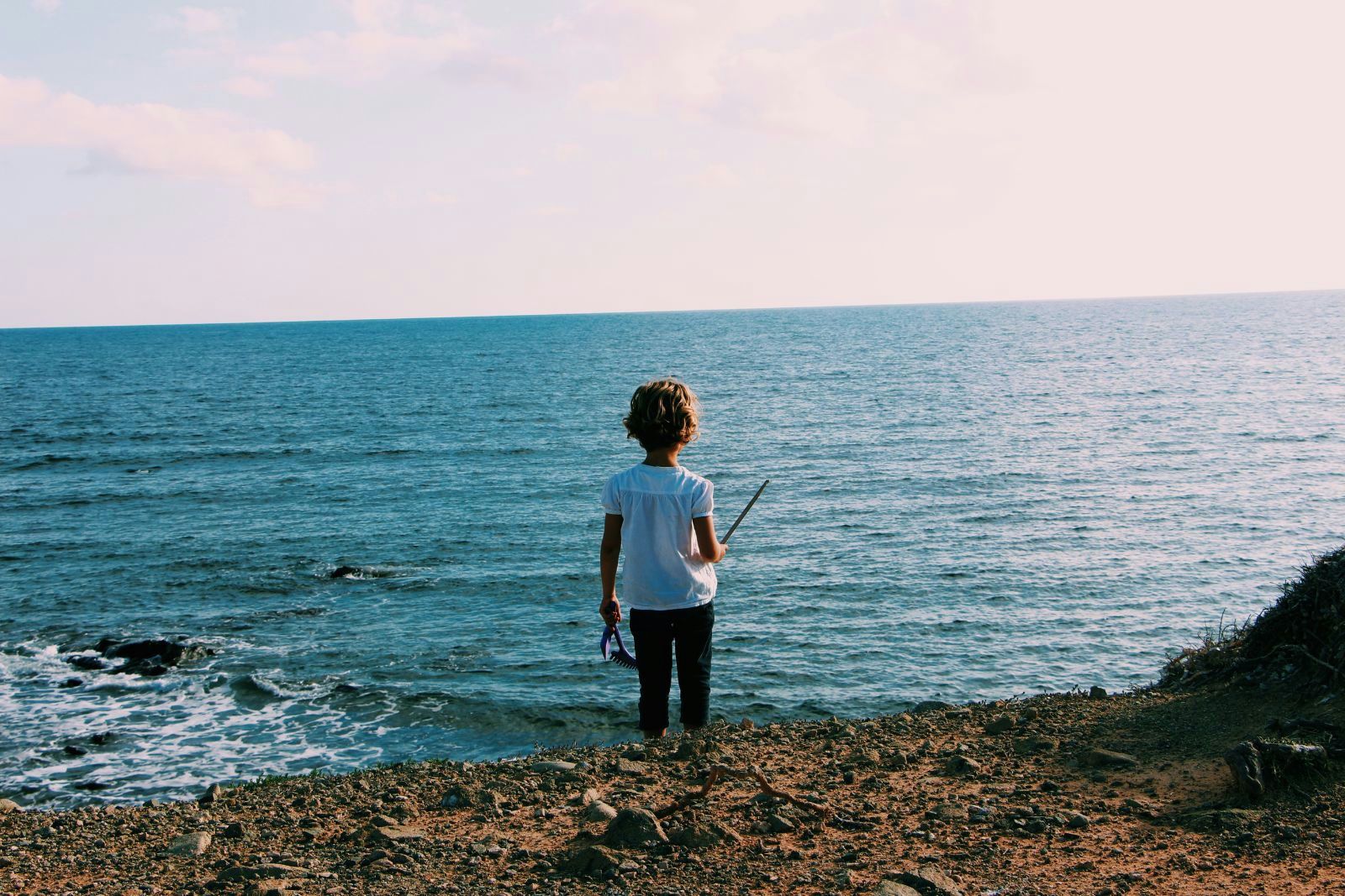Raise children as good stewards of the ocean A young child stands alone on a rocky shore, facing the vast ocean, to illustrate the blog post How to raise children as ocean stewards